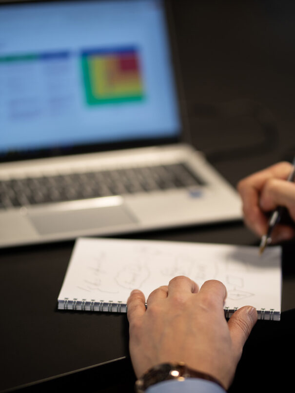 hand writing a note in front of a laptop
